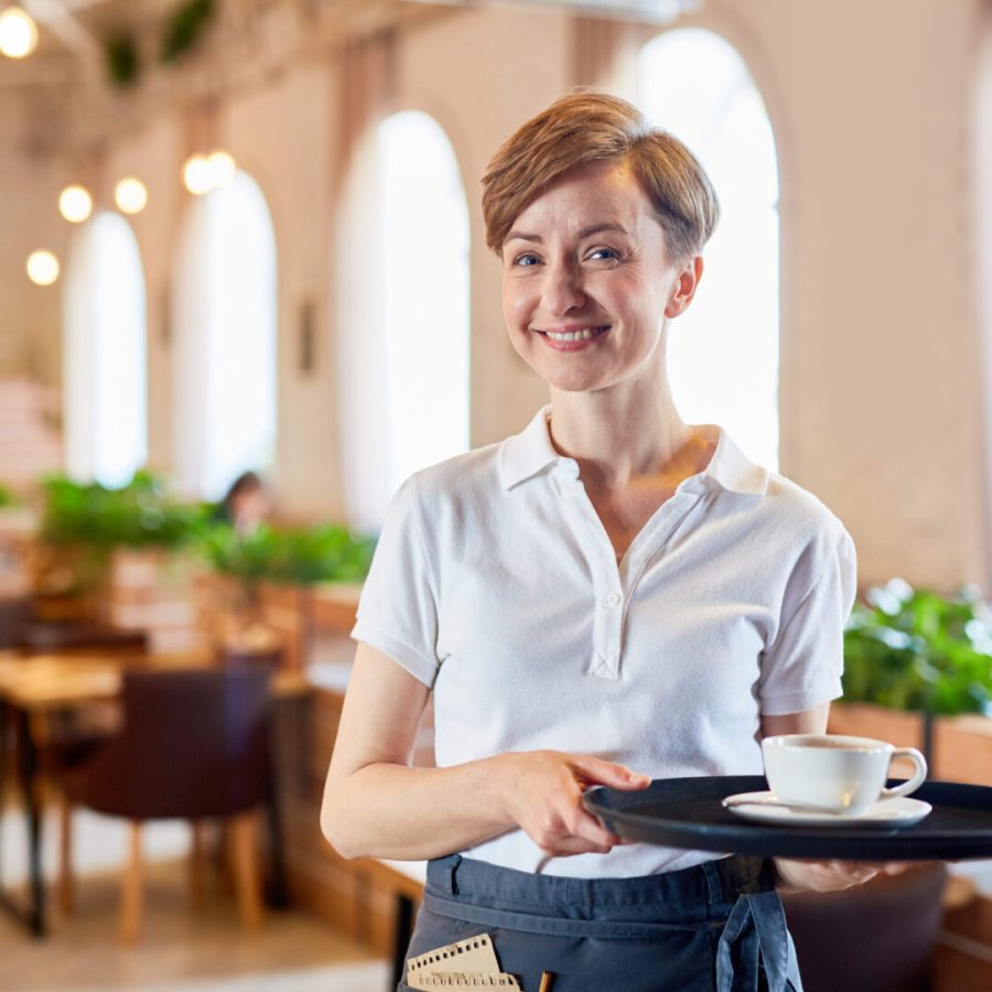 Service of restaurant Smiling sesrvant in uniform bringing cup of coffee to visitor of restaurant